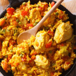 A delicious and hearty Latin American dish featuring tender chicken pieces cooked with seasoned rice, colorful bell peppers, peas, and a savory tomato-based sauce.