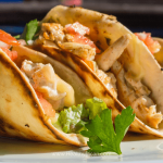 Delicious chicken and avocado tacos on a rustic wooden table, garnished with fresh cilantro and lime slices, perfect for a flavorful meal.