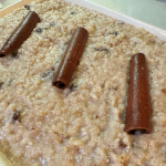 A close-up of a creamy dessert topped with three rolled cinnamon sticks, featuring a smooth, textured surface.