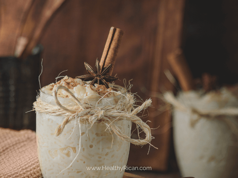 A close-up of a glass filled with creamy Arroz con Dulce, a traditional Puerto Rican holiday dessert, garnished with cinnamon sticks and star anise, set against a rustic background.