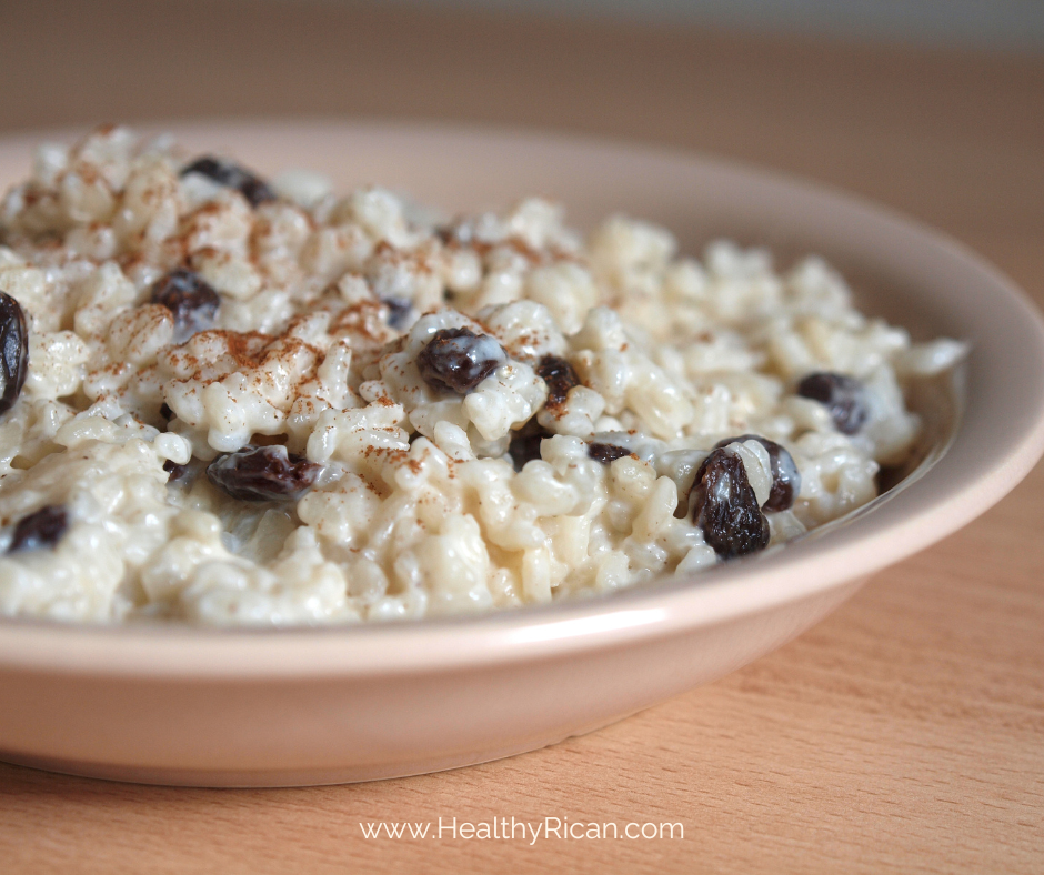 A close-up view of a beige dish filled with creamy rice, sprinkled with cinnamon and dotted with dark raisins.